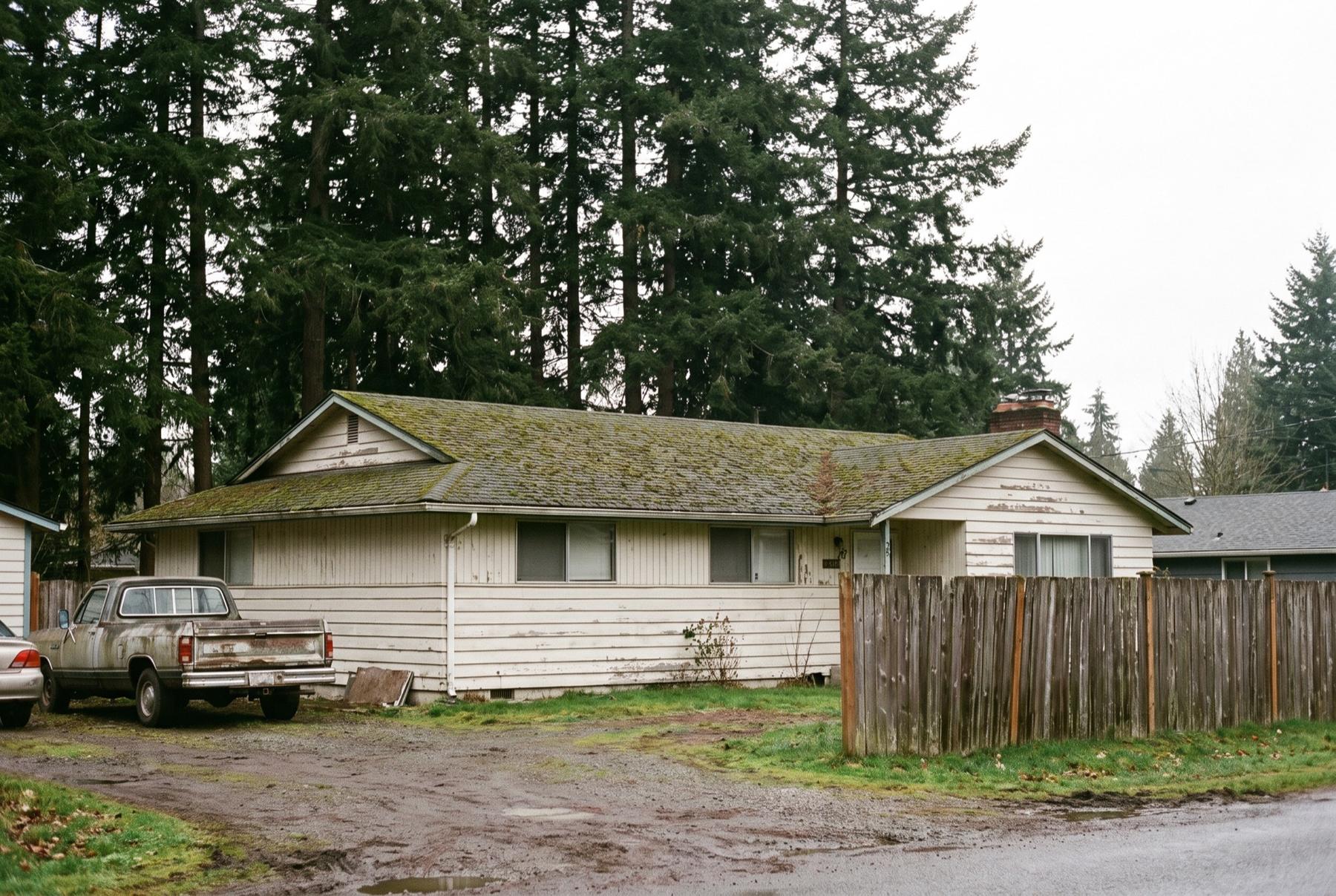 Older rambler with a mossy roof and tall Douglas firs behind it in Spanaway